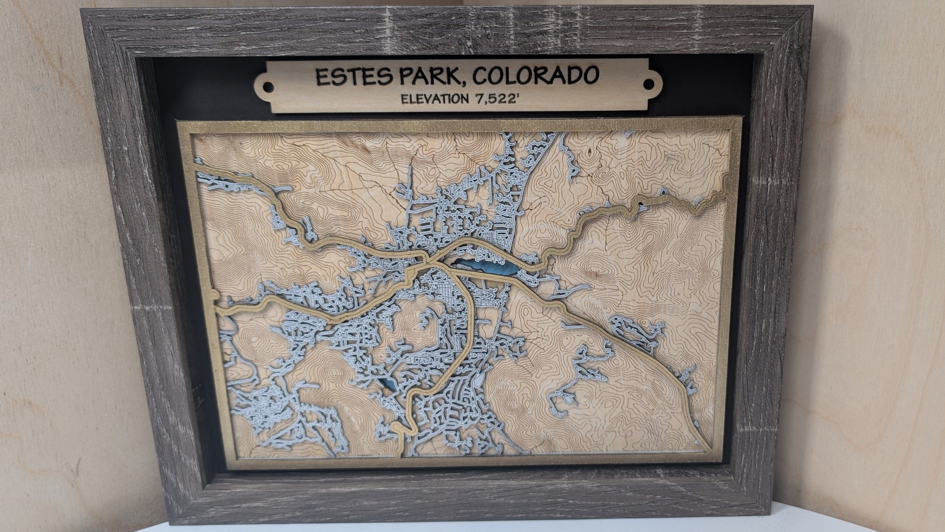 Framed topographic map of Estes Park, Colorado on a wooden surface.