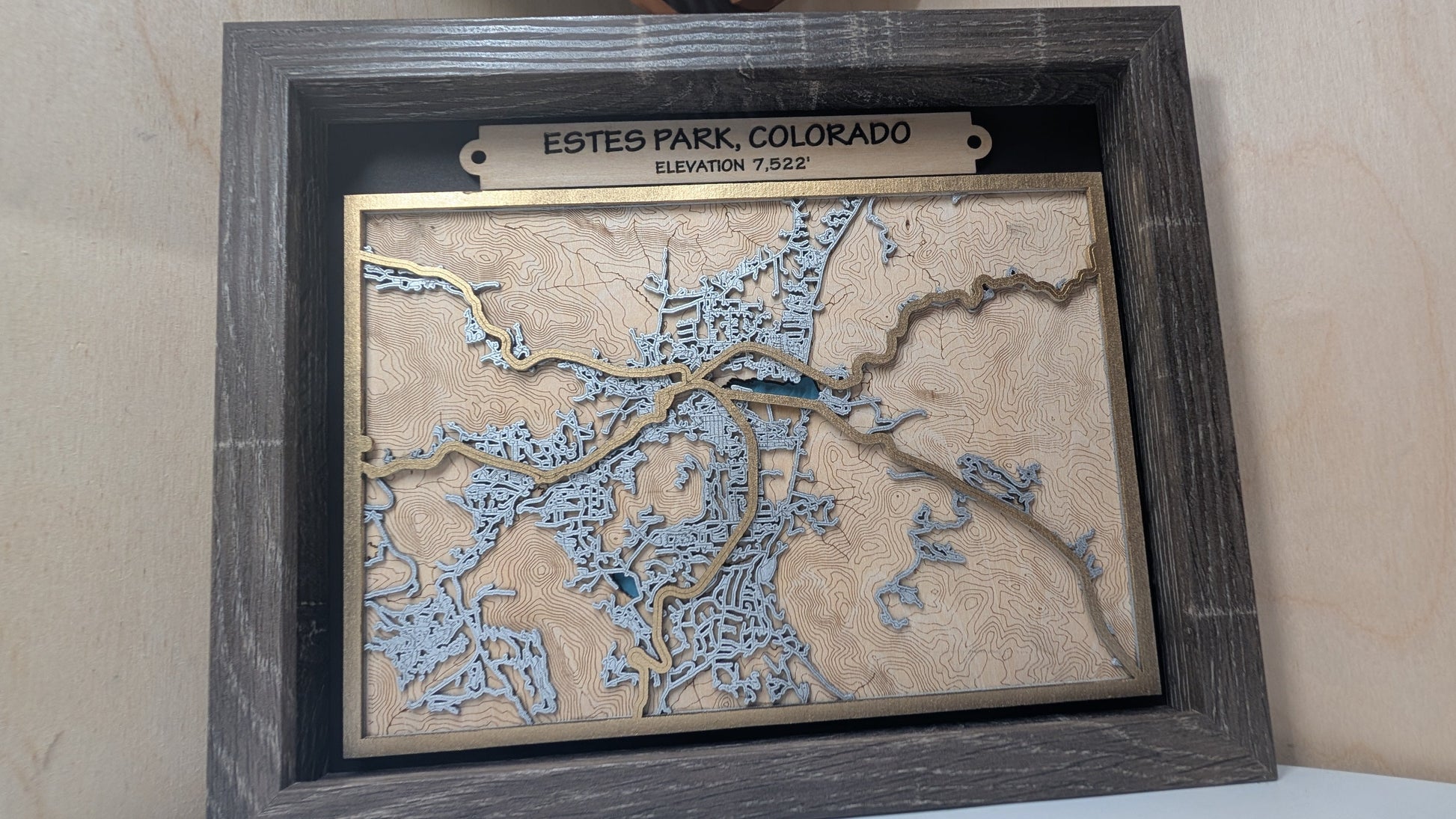 Framed topographic map of Estes Park, Colorado on a wooden surface.