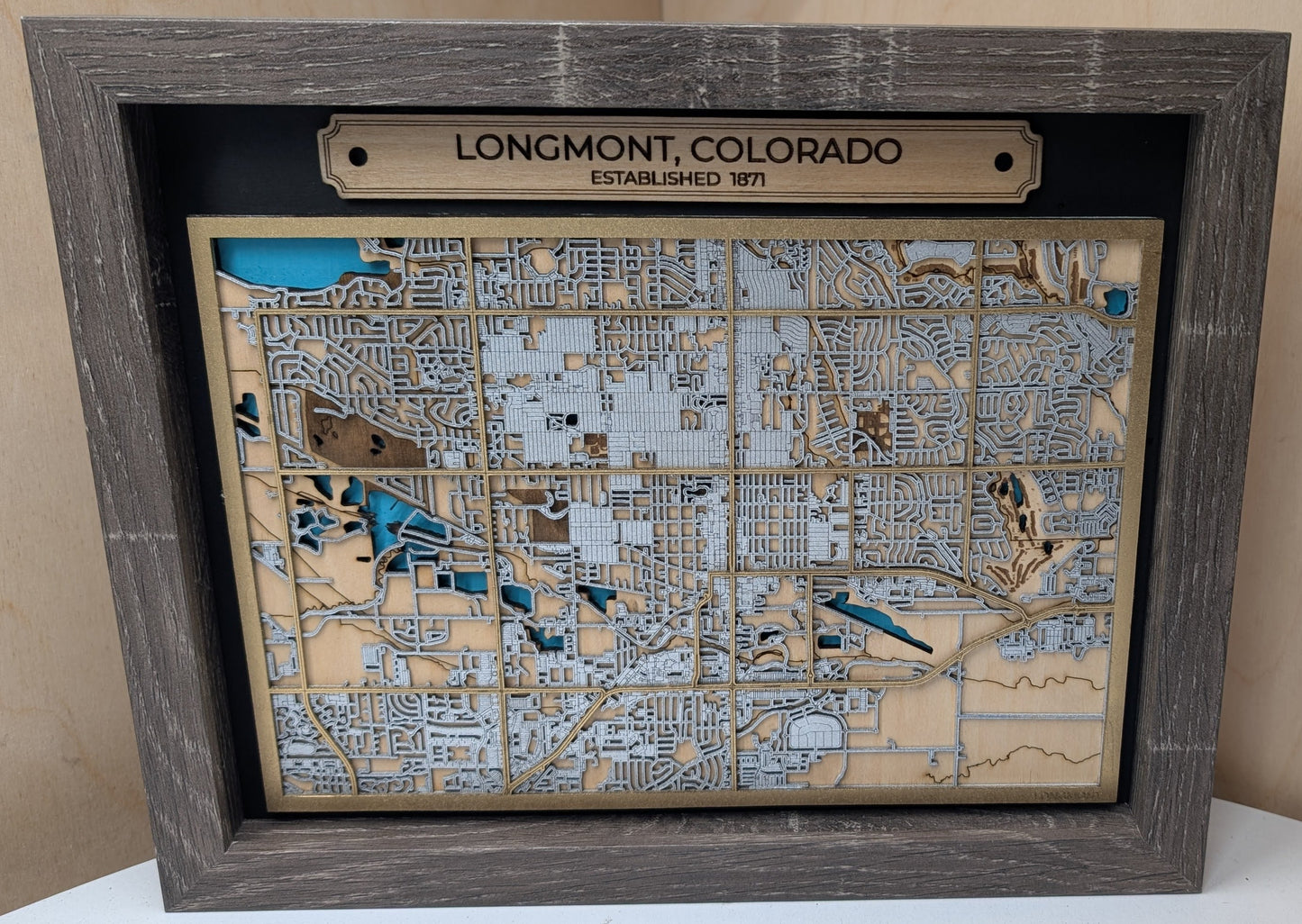 Wooden map of Longmont, Colorado with a wooden frame on a light wood background