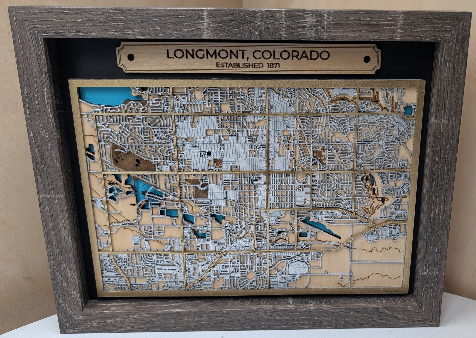 Wooden map of Longmont, Colorado with a wooden frame on a light wood background
