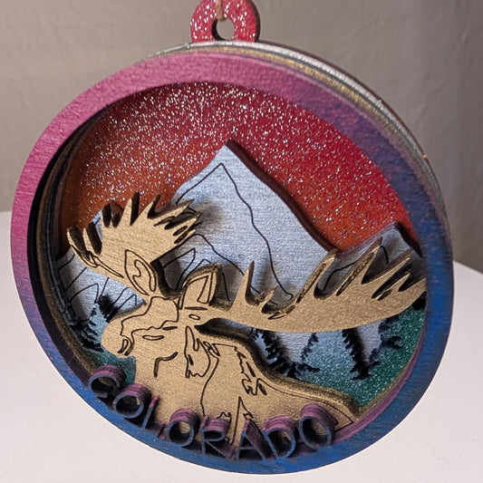 Decorative ornament with a moose and mountain design on a white surface.